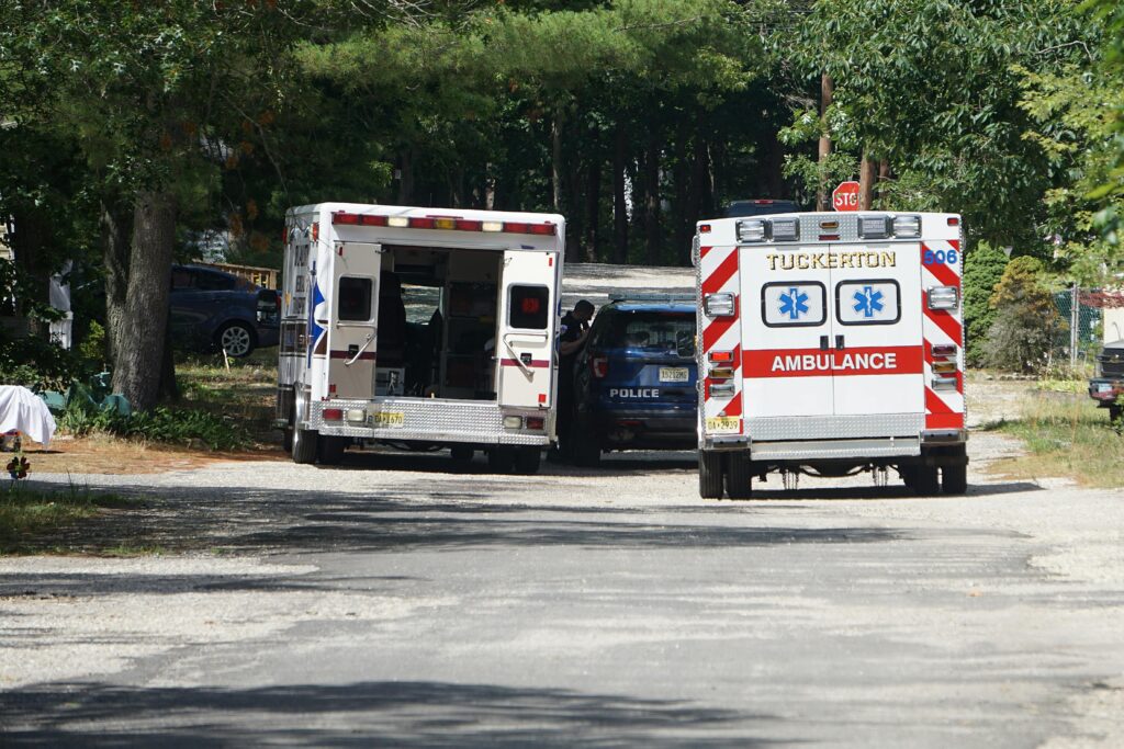 Ambulances and a police car on a tree-lined road responding to an emergency.