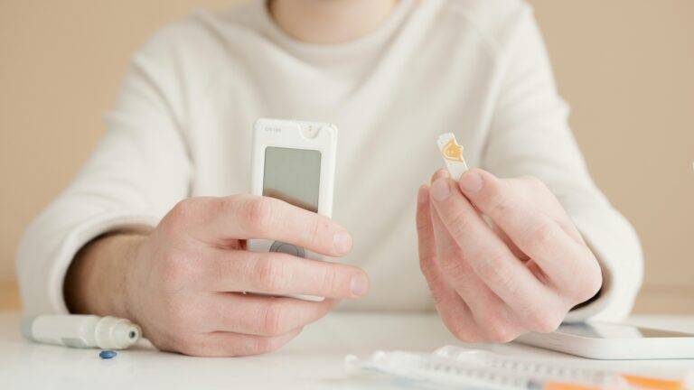 Close-up of hands using a glucometer for blood sugar testing indoors.