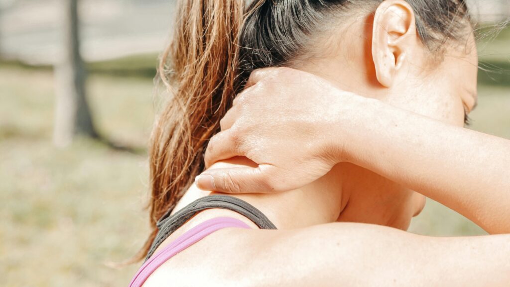 A woman massages her neck outdoors, relieving discomfort and tension.